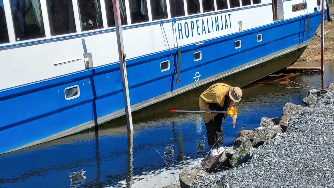 Taustalla matkustajalaiva, etualalla henkilö ottaa vesinäytettä.